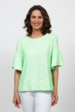 Top Ligne Neon Flowers Flounce Tee in Green. Green textured velour flours on a white background. Crew neck tee with elbow length sleeve with ruffled cuff. A line shape. Relaxed fit._35730168316104